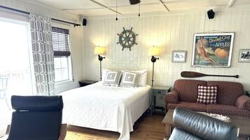A room with a bed, two chairs, a sofa, a table, and a wall with a ship's wheel and a vintage magazine.
