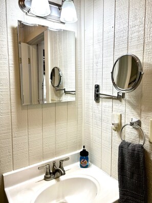 A bathroom with a white sink, two mirrors, a towel ring, and a soap dispenser. - Lakeside Cabin With Your Own Personal Beach and Expansive Lake View (Point Blank)