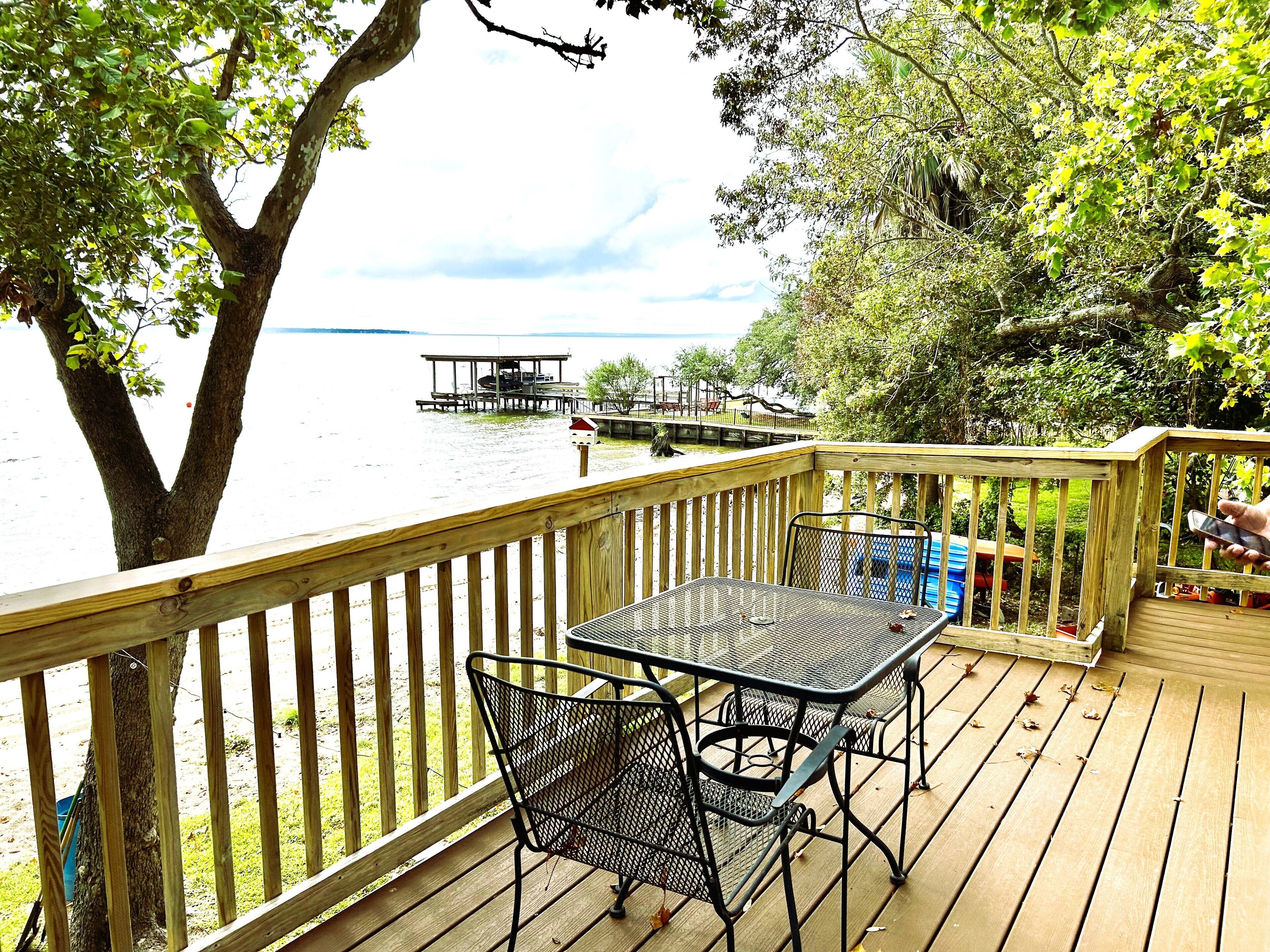 A wooden deck with a table and chairs overlooking a lake, a dock, and a boat.