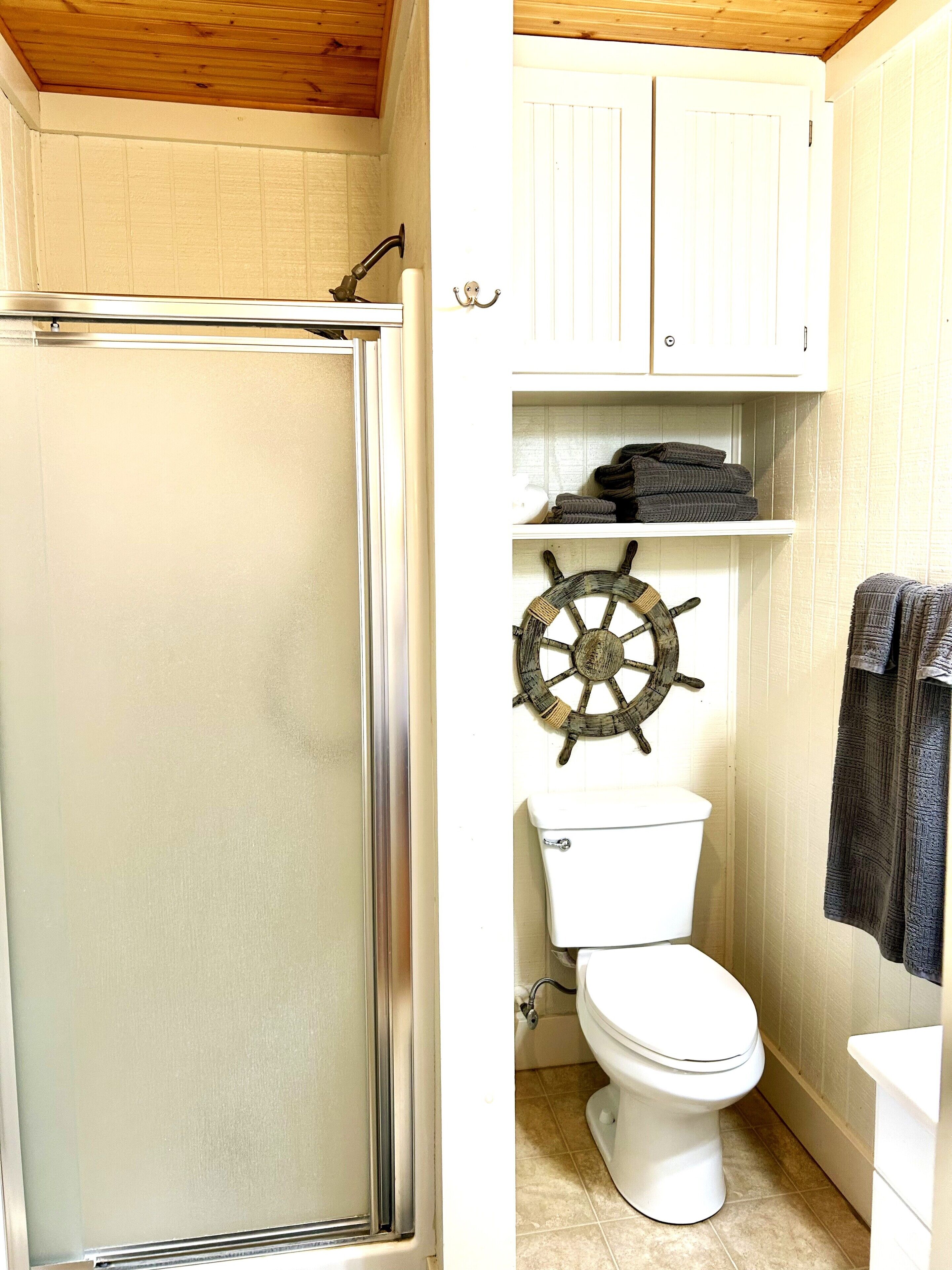 Une salle de bain équipée d’une douche, de toilettes et décorée avec un volant de navire.