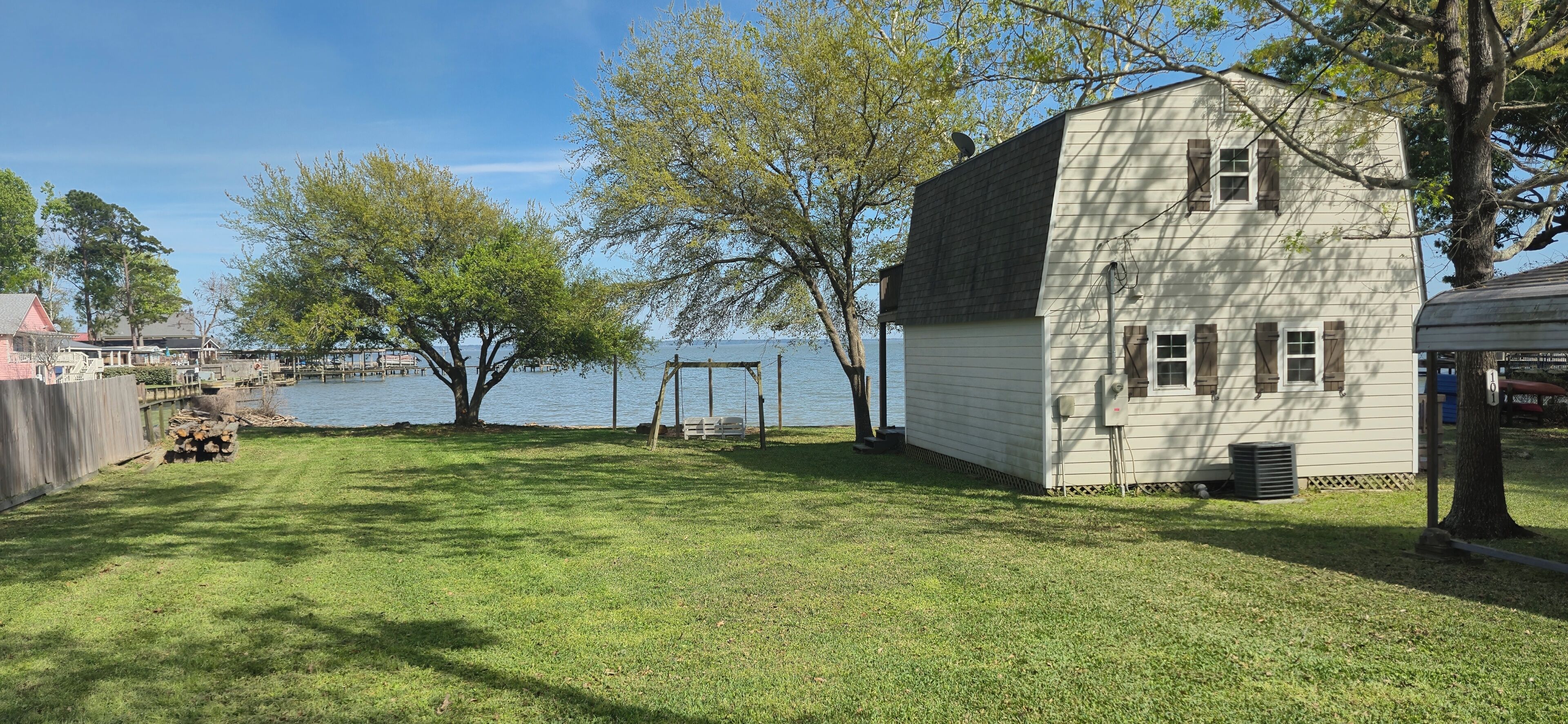 A house with a yard by a lake, a swing set, and a dock.