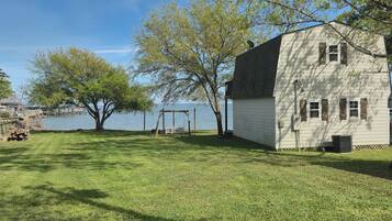 A house with a yard by a lake, a swing set, and a dock.