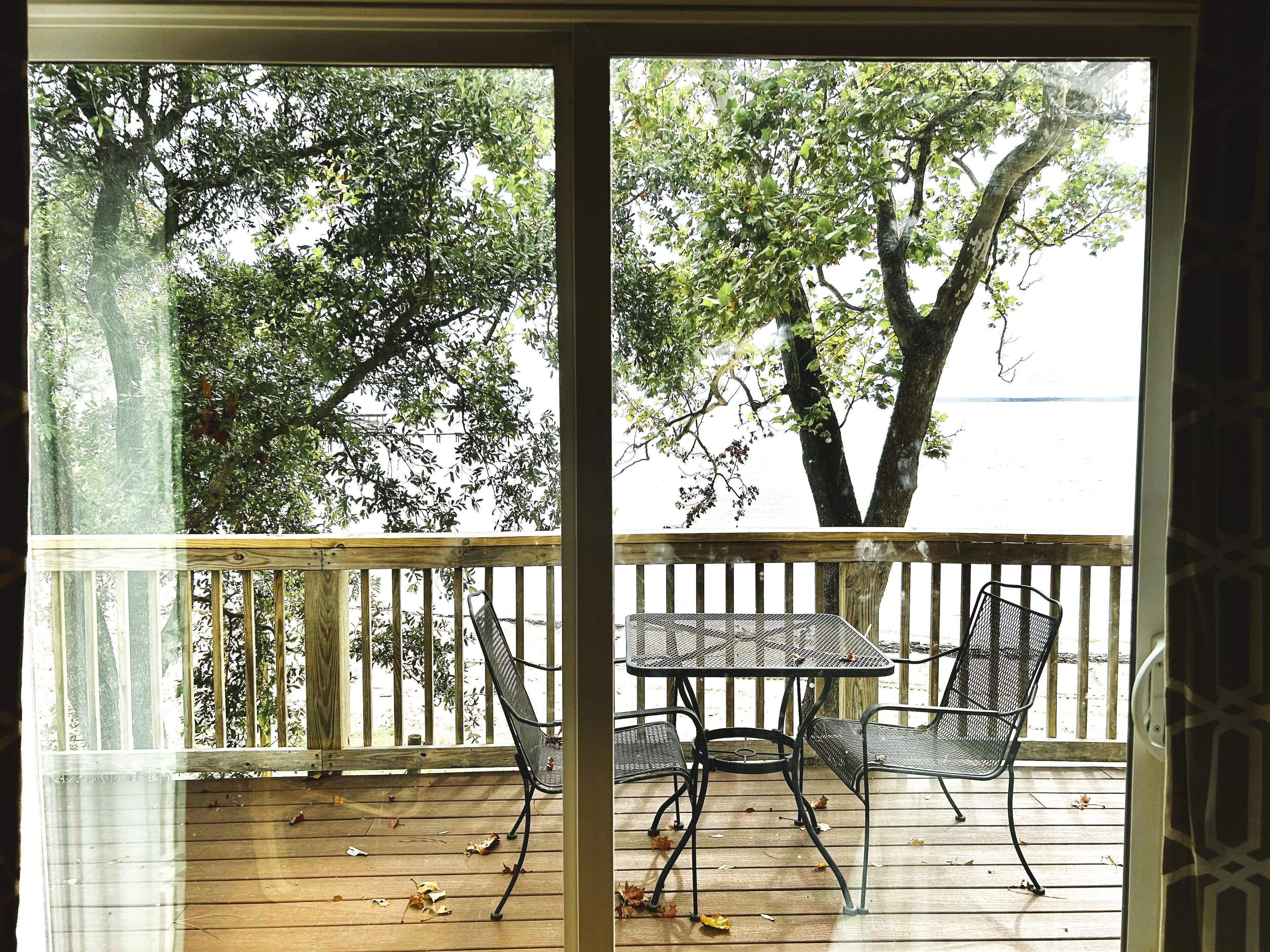 A wooden deck with a metal table and chairs, overlooking a body of water and trees.