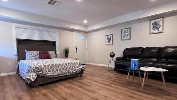 A bedroom with a bed, a black leather couch, and a small table.