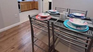 A dining area with a table set for four, a kitchen in the background, and an air conditioning unit on the wall.