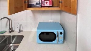 A kitchen with a blue microwave, a stainless steel sink, and wooden cabinets.