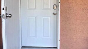 A white door with a small window at the top, a doorknob, and a doorbell.