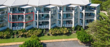 A modern multi-story hotel with a glass facade, located near a beach with a clear view of the ocean.
