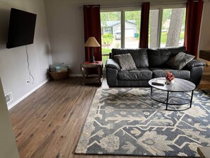 A living room with a black leather sofa, a round coffee table, a patterned rug, and a lamp. - Cedarwood Chateau (Cambridge)