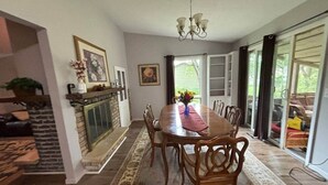 A dining room with a long wooden table, chairs, a chandelier, a fireplace, and a view through large glass doors. - Cedarwood Chateau (Cambridge)