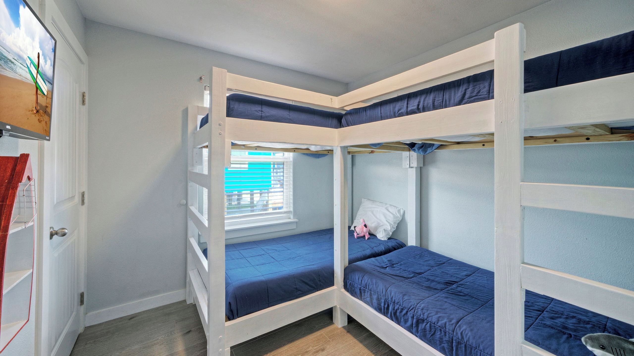 A room with bunk beds, a window with blinds, a door with a red towel, and a small window with a view of the outside.