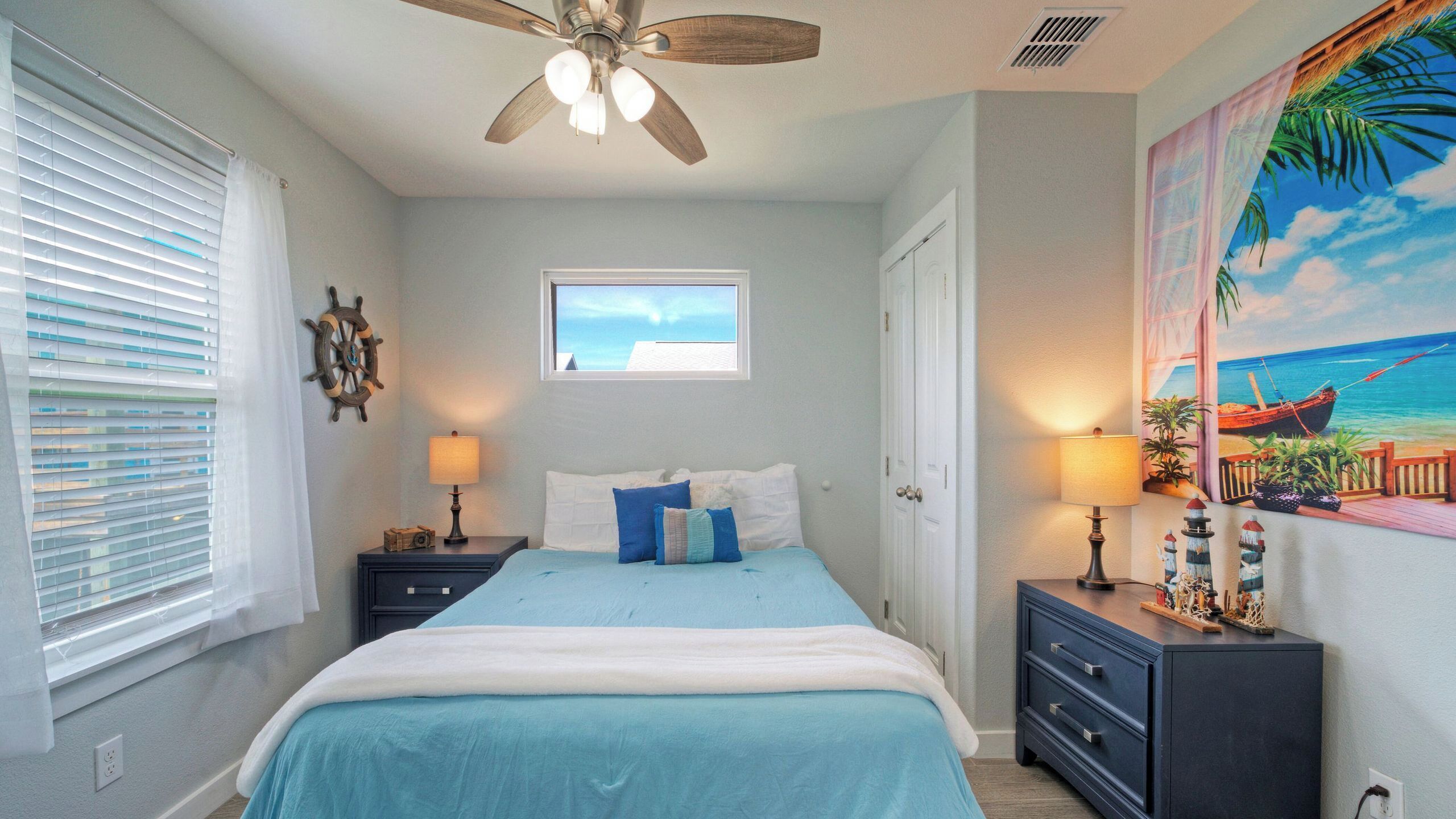 Une chambre à coucher comprenant un lit, deux tables de chevet, un ventilateur de plafond, une fenêtre et un tableau mural.