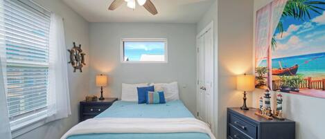 Une chambre à coucher comprenant un lit, deux tables de chevet, un ventilateur de plafond, une fenêtre et un tableau mural.