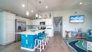 Uma cozinha moderna com uma ilha central, armários brancos, eletrodomésticos de aço inoxidável e banquetas azuis.