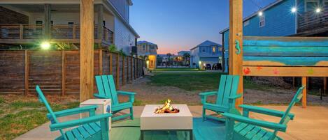 An outdoor seating area with two chairs and a table, a fire pit, and a view of houses in the background.