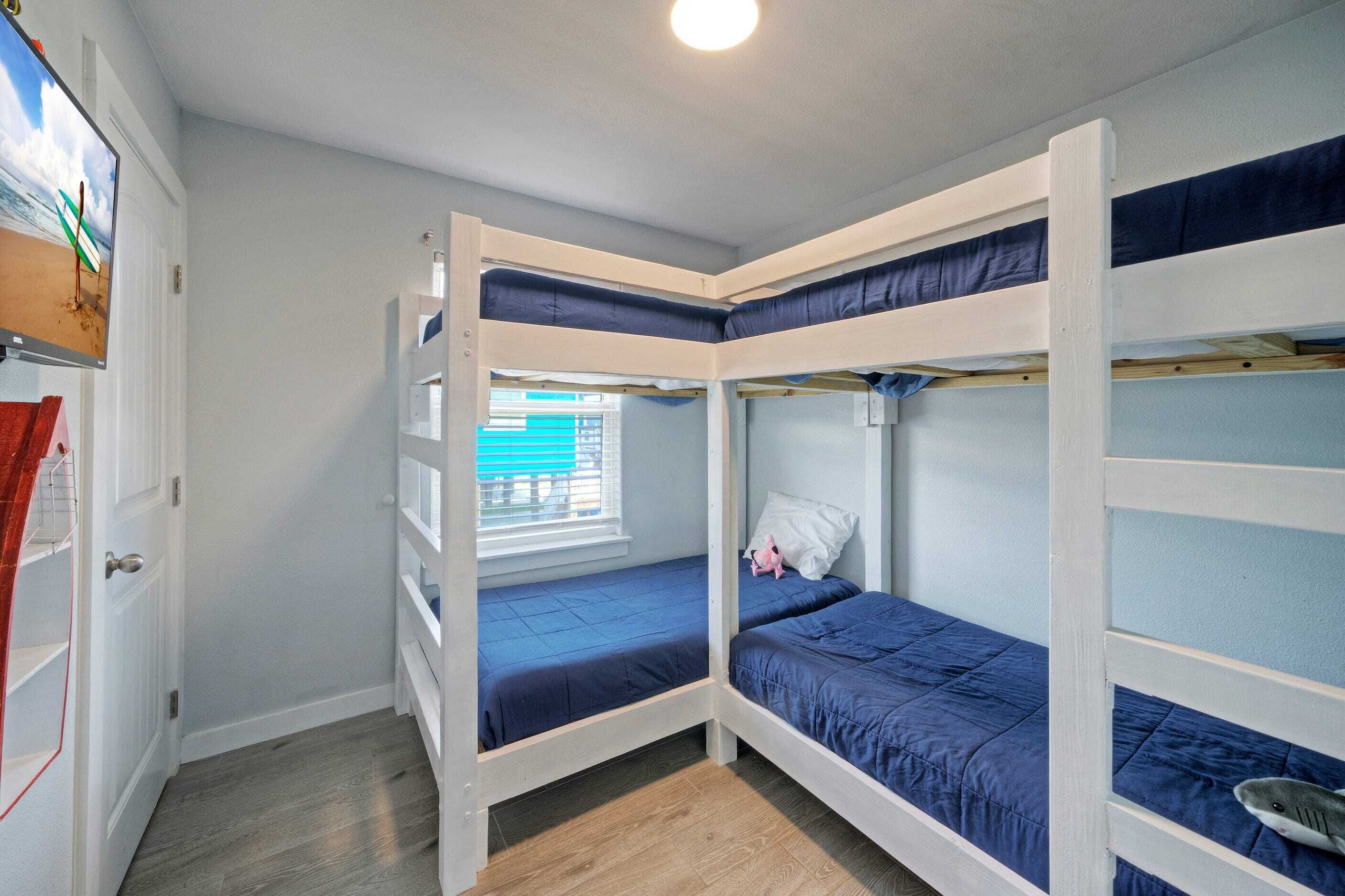 A bunk bed room with a TV on the left, a window with blinds, and a door with a red curtain.