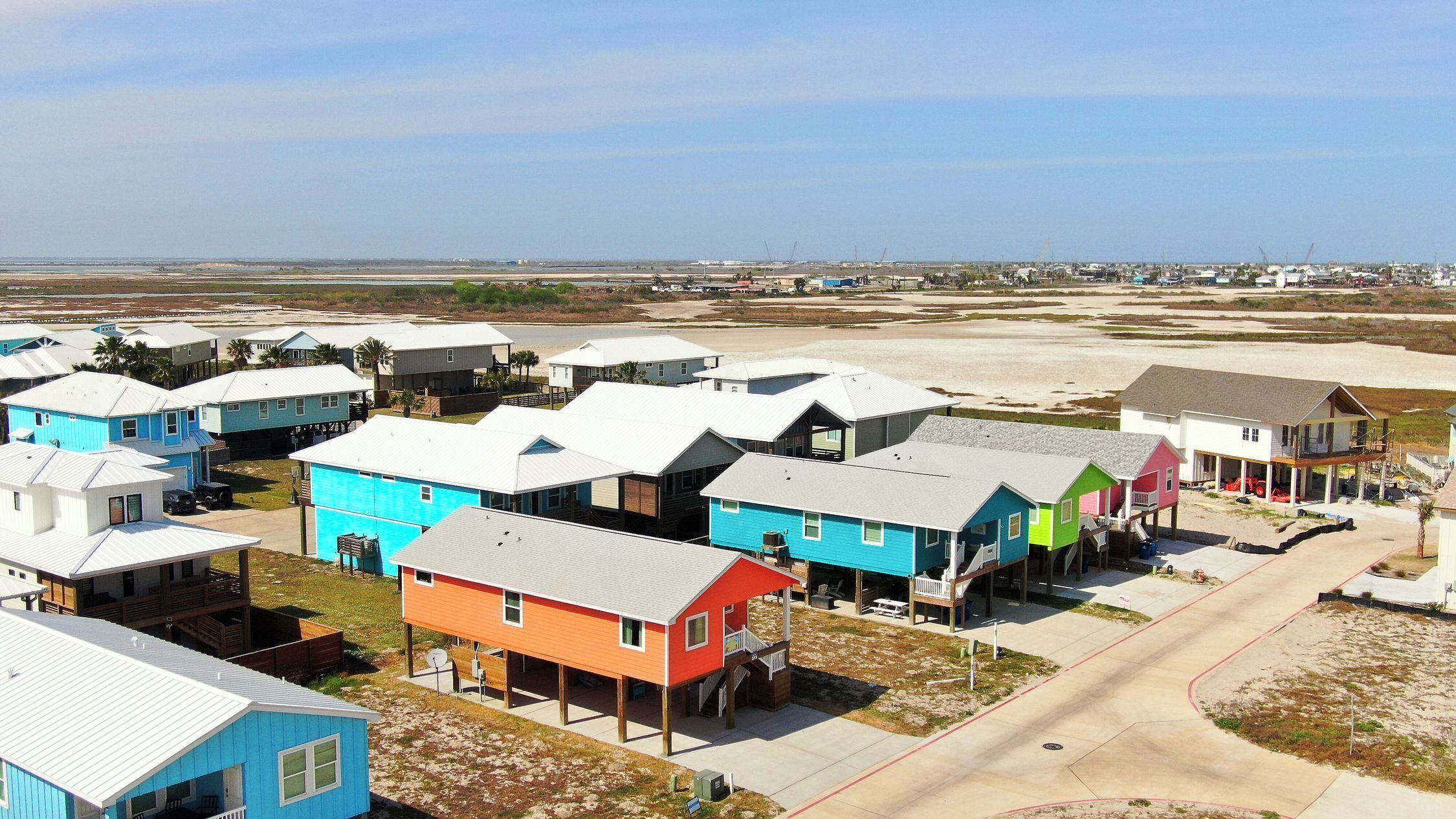 Una zona residencial costera con casas coloridas, una playa arenosa y un cielo despejado.