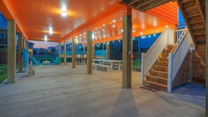 Een overdekt terras buiten, met houten pilaren, lichtslingers en zithoeken.