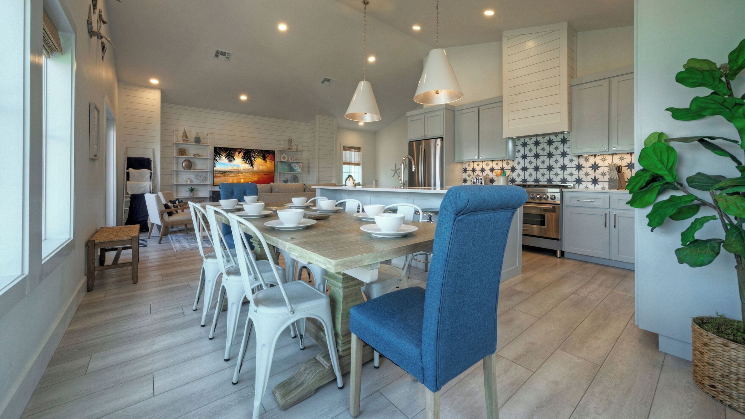 A modern kitchen with white cabinets, a dining area with a wooden table and white chairs, and a large window.