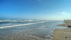 A beach with waves, a person walking, and a clear sky. - Luxury 4bdr Beach Retreat w/ Private Pool Walk to Dining + Shops Shore Thang (Port Aransas)