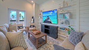 A living room with a TV, wooden shelves, and a view of the ocean. - Luxury 4bdr Beach Retreat w/ Private Pool Walk to Dining + Shops Shore Thang (Port Aransas)