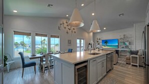 A spacious kitchen with a large island, modern pendant lights, and a view of the ocean through large windows. - Luxury 4bdr Beach Retreat w/ Private Pool Walk to Dining + Shops Shore Thang (Port Aransas)