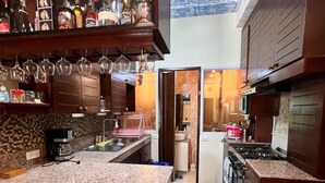 A kitchen with granite countertops, a stove, and a microwave. There is a bar area with bottles and glasses.
