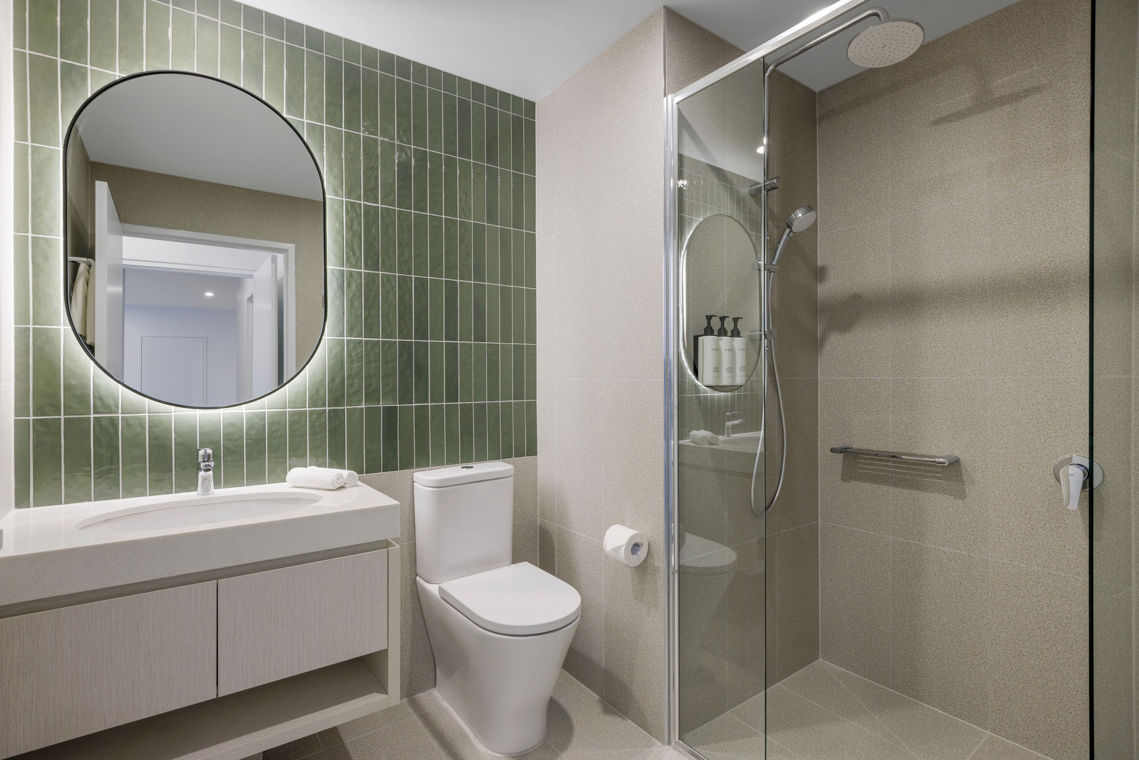 A modern bathroom with a glass-enclosed shower, a round mirror, and a toilet.