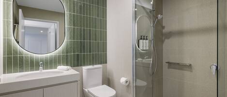 A modern bathroom with a glass-enclosed shower, a round mirror, and a toilet.