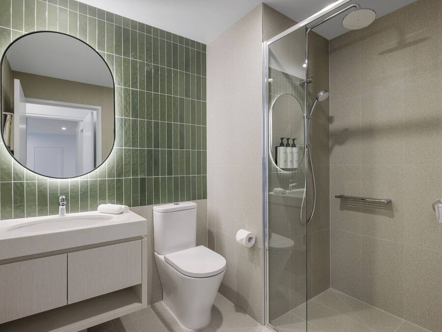 Een moderne badkamer met een douchecabine van glas, een ronde spiegel en een toilet.