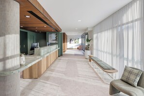 Un espace d’accueil moderne, doté d’un comptoir de réception en bois, d’un banc et d’une grande fenêtre agrémentée de rideaux légers.