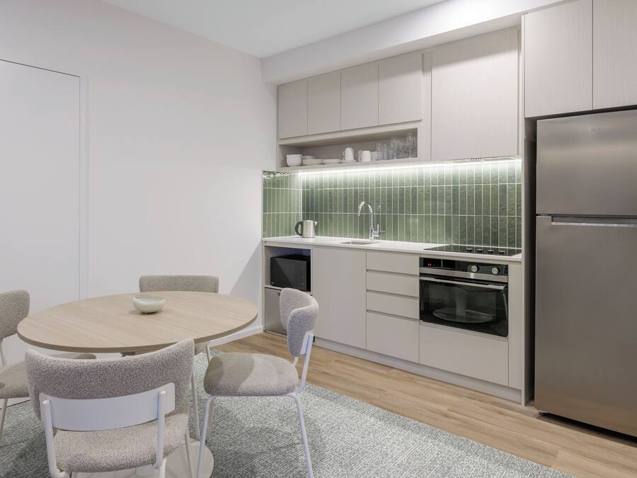 Een moderne keuken met een ronde eettafel, stoelen, een koelkast, oven en een magnetron.