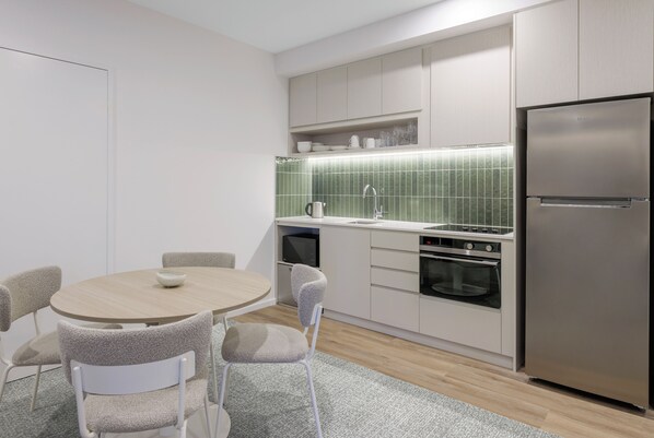 Cozinha moderna com mesa de jantar redonda, cadeiras, geladeira, forno e micro-ondas.