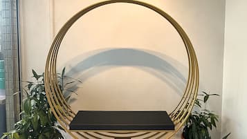 A circular seating area with a black bench, surrounded by a gold frame, and potted plants on either side. A sign above reads 'BLANC INNSG.'