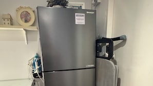 A compact, stainless steel refrigerator with a freezer compartment on top, situated in a small kitchen area with a white countertop and a blue rug on the floor. - Blanc Inn (Singapore)