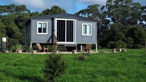 A compact, two-story cabin with a flat roof, large sliding glass doors, and a small porch area.