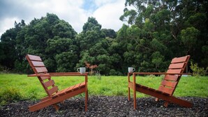 Two wooden lounge chairs with metal frames, placed on a gravel surface, with a table between them and a white mug on each chair.