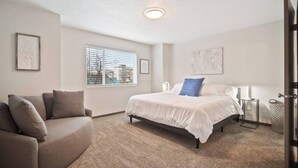 A bedroom with a bed, a couch, a window with blinds, and a door. - Your stay will include the entire Unit A to yourself (Spokane)
