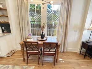 Een eethoek met een houten tafel, twee stoelen, een vaas met bloemen, een schaal en een raam met een grillwerkontwerp.