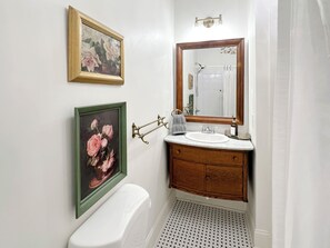 Een badkamer met een toilet, een wastafel met spiegel en twee florale schilderijen in lijsten aan de muur.