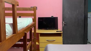 Ein Stockbett mit Holzrahmen, ein kleiner Schreibtisch mit Fernseher und ein Kleiderschrank in einem Zimmer mit rosafarbenen Wänden.