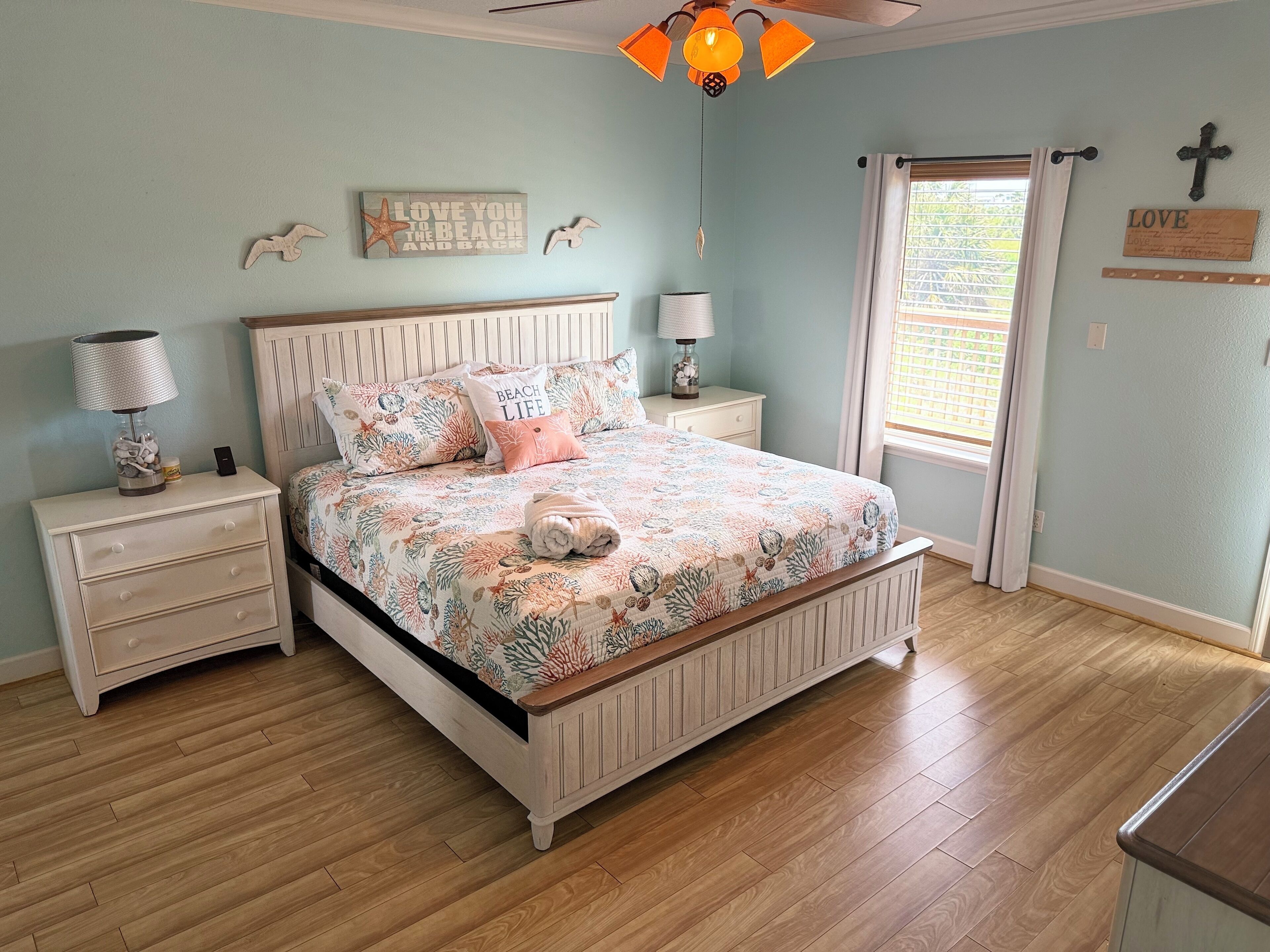 A bedroom with a wooden bed, white nightstands, a ceiling fan, and a window with curtains.