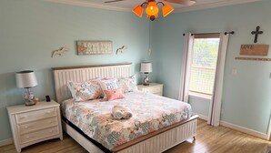 Ein Schlafzimmer mit einem Holzbett, weißen Nachttischen, einem Deckenventilator und einem Fenster mit Vorhängen.