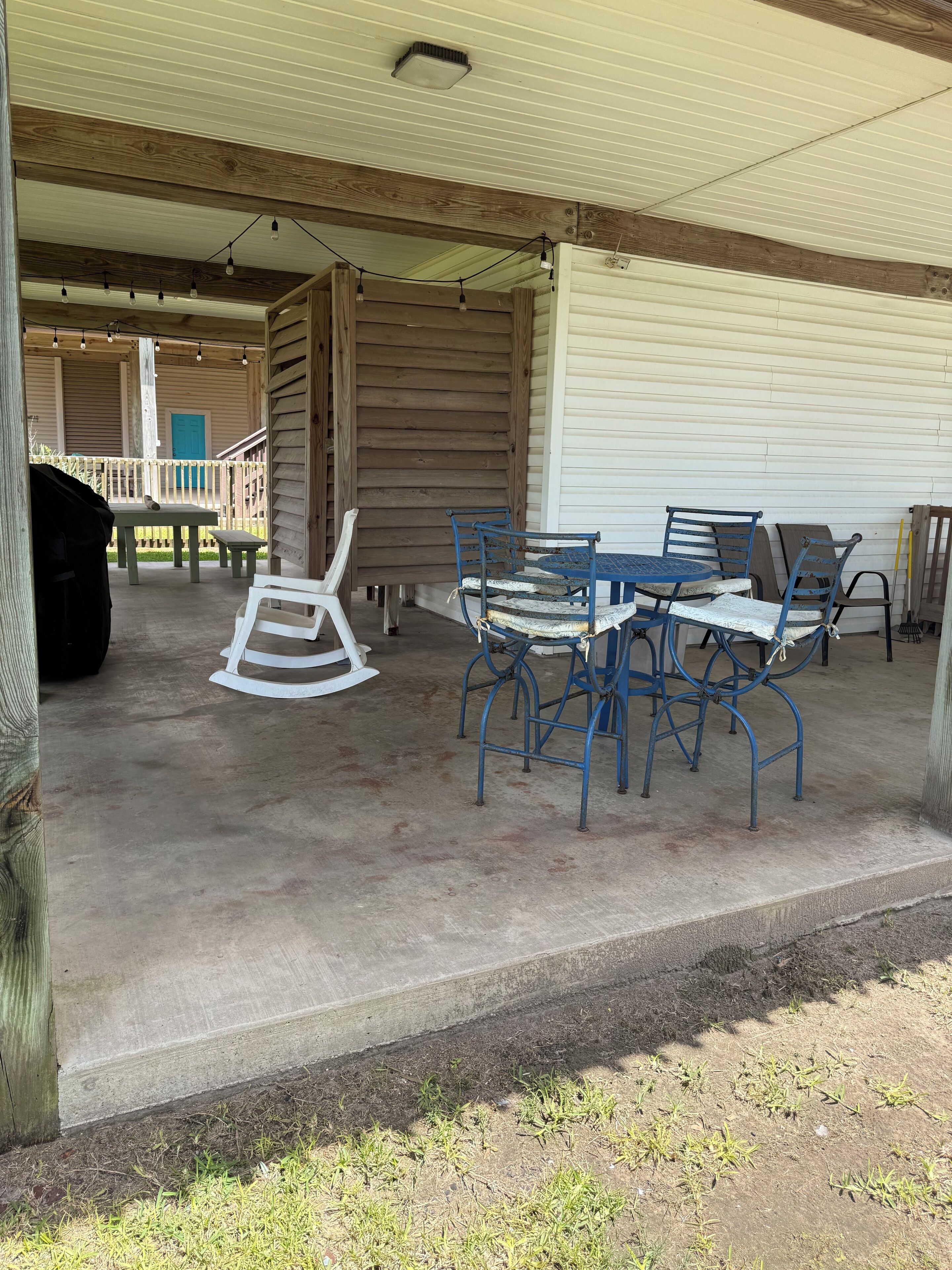 An outdoor covered patio area with a table and chairs, a rocking chair, and a barbecue grill.