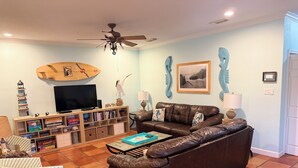 Ein Wohnzimmer mit braunem Ledersofa, einem Fernseher, einem Bücherregal und einem Deckenventilator.