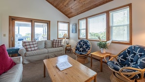 A cozy living room with a wooden ceiling, a sofa, a chair, a coffee table, and large windows.
