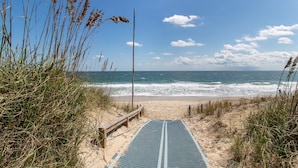 A beach path leading to the ocean with a wooden fence and a metal guardrail.