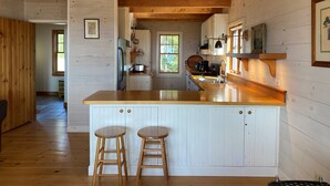 Interior de una cabaña de madera con una cocina que incluye una isla de madera con taburetes, un refrigerador y un fregadero.