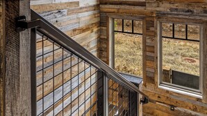 A wooden interior with a staircase, large windows, and a hanging light fixture.
