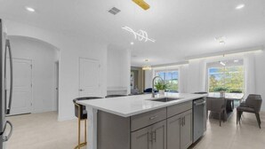 A modern kitchen with a large island, white cabinetry, and a dining area with a table and chairs. - Magic & Adventure in This Stunning home in CG (Davenport)